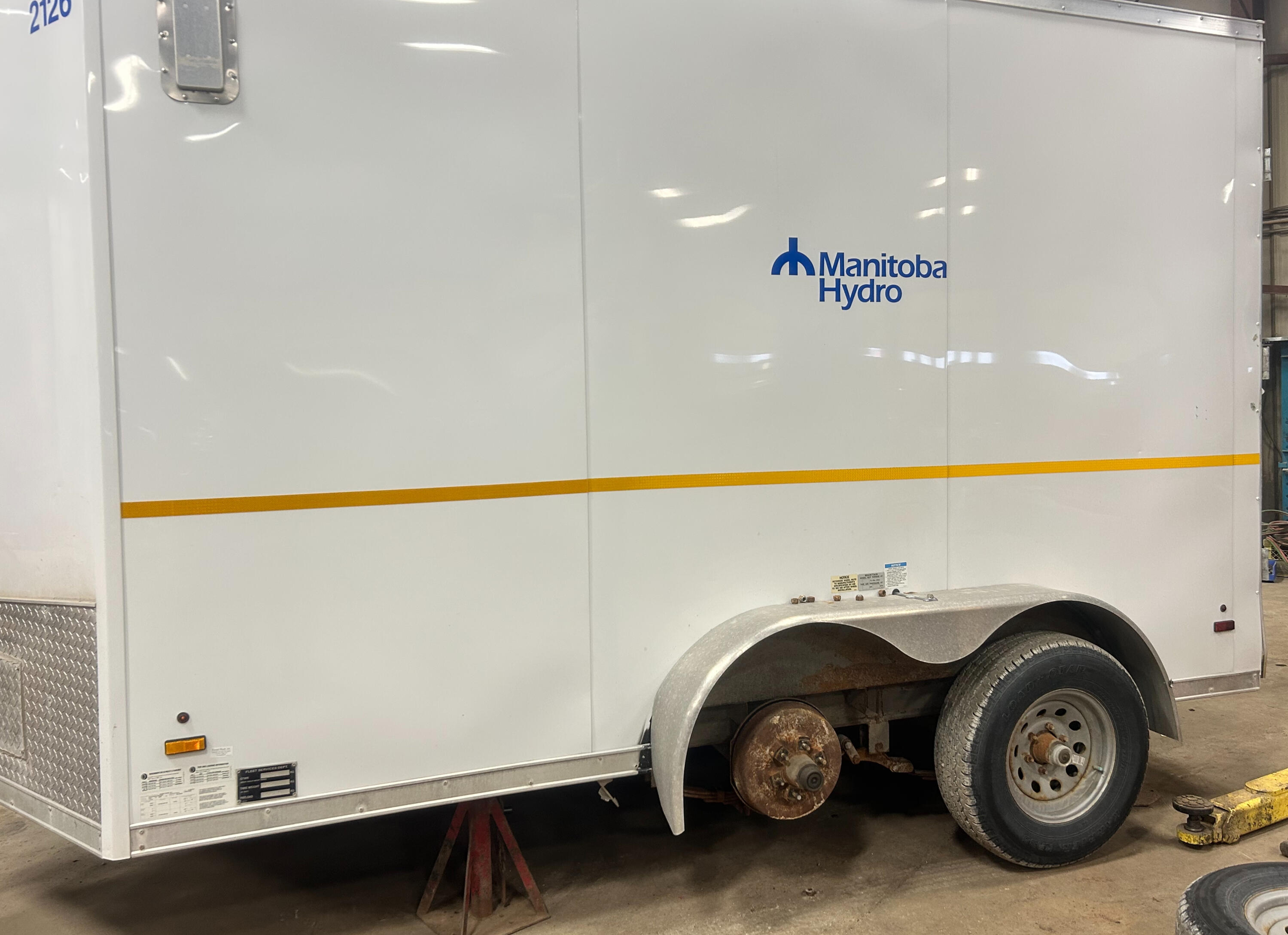 Commercial enclosed trailer receiving suspension and axle repairs at Standard Auto Spring Works in Winnipeg, Manitoba. Trailer axle replacement, leaf spring repair, wheel bearings, U-bolts, and suspension service.