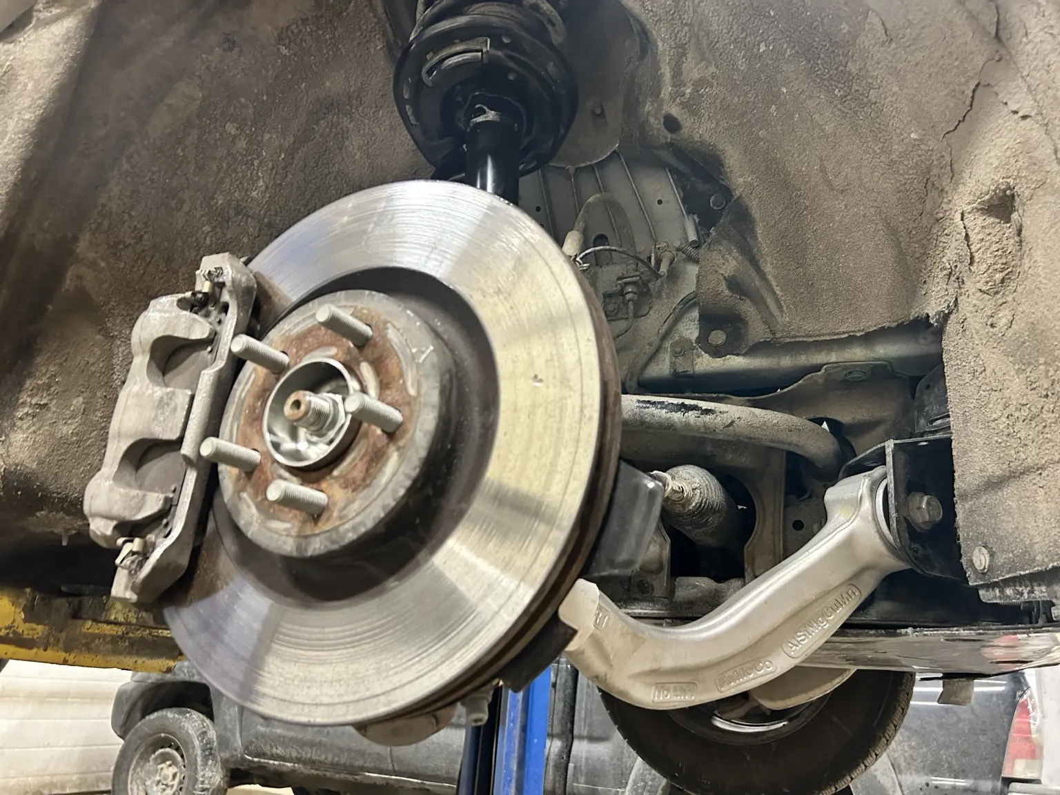 Front brake rotor, caliper, strut, control arm and steering components exposed for inspection